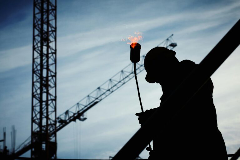 Silhouette of a worker welding steel beside a construction crane