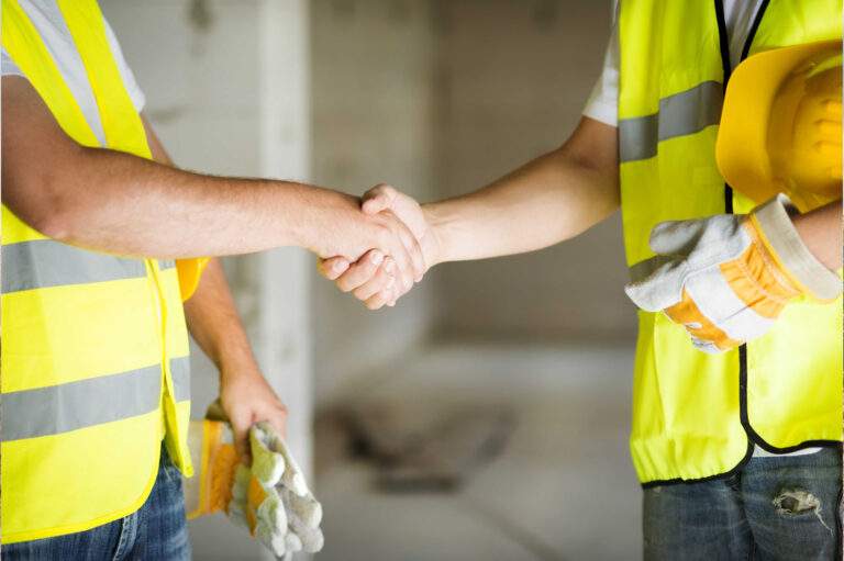 Two workers in safety vests shaking hands on a job site