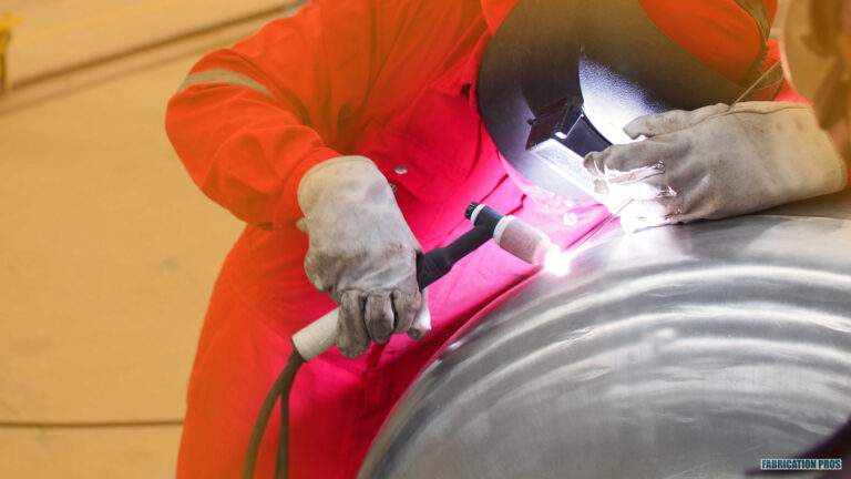 Welder in orange coveralls welding a large curved steel vessel