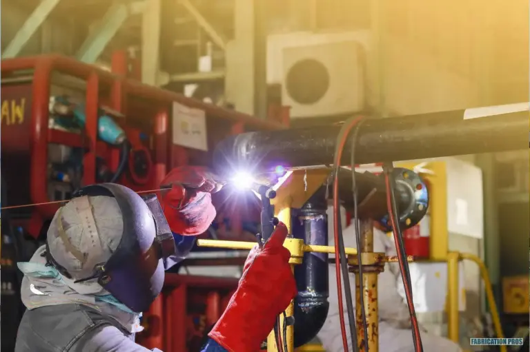 Welder in a hood welding piping at an industrial site