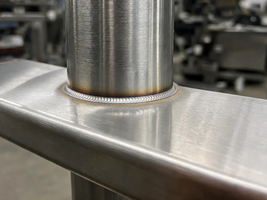 Close-up of a TIG weld around the base of a brushed stainless steel handrail post