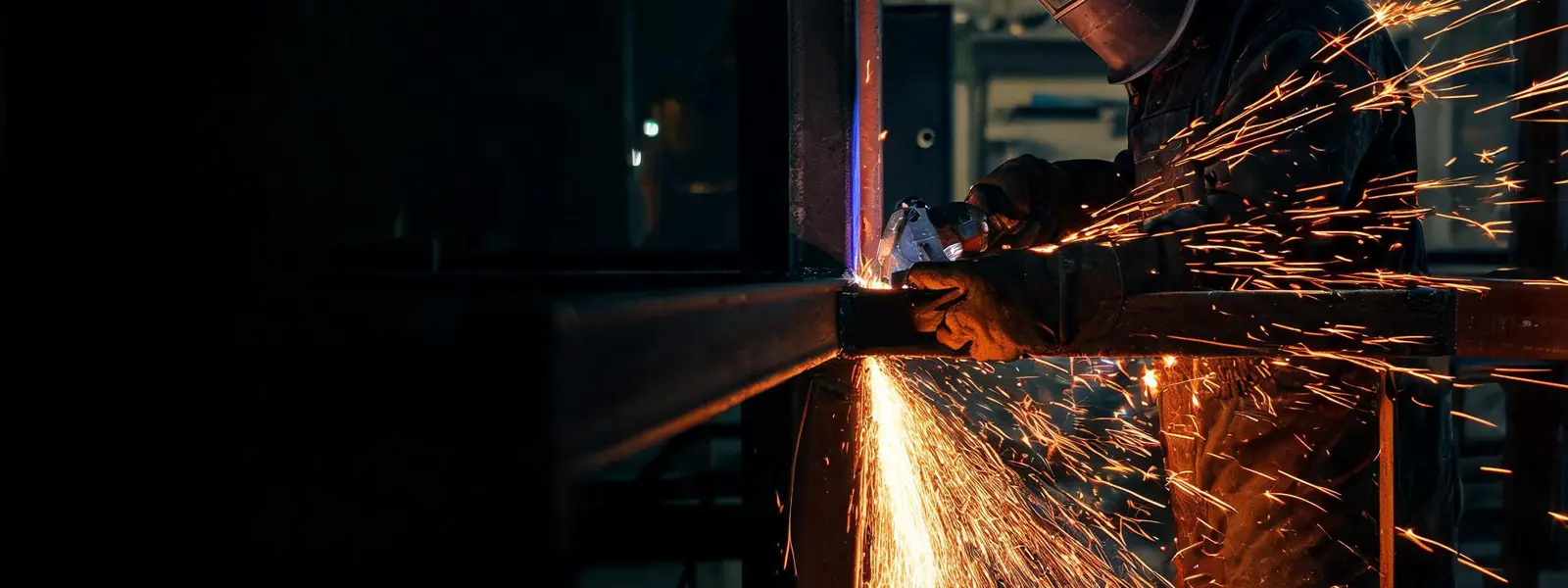Welder grinding a steel frame with a shower of sparks in a dark shop