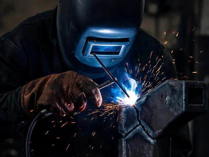 Welder repairing a cracked steel bracket with a stick welding arc